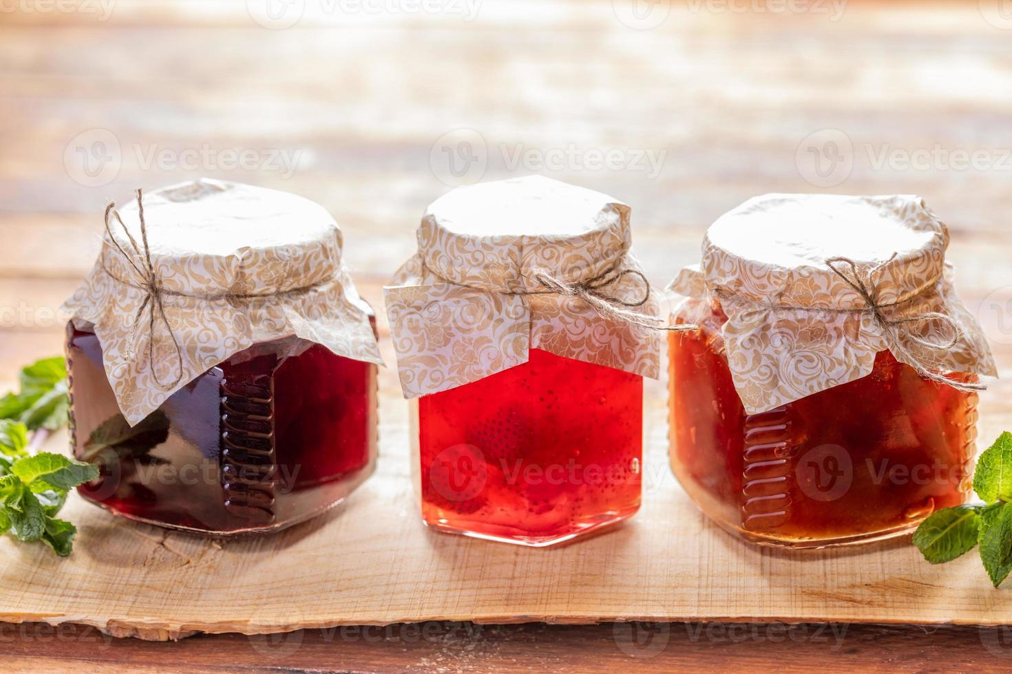 Close-up three glass jars with homemade  jam are standing in row on wooden background. photo