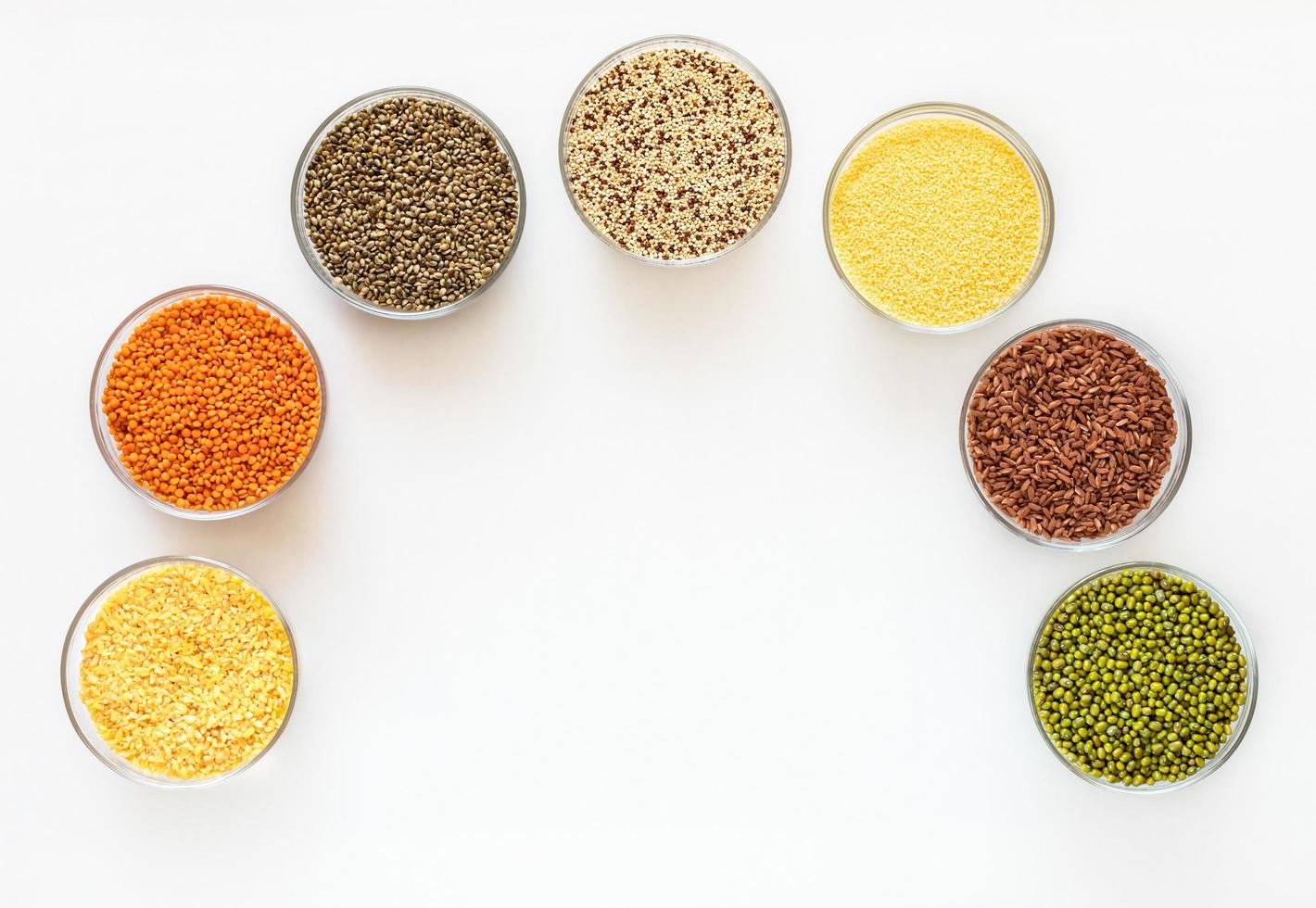 Flat lay glass bowls with superfoods are standing as arc on white background with copy space in middle. photo