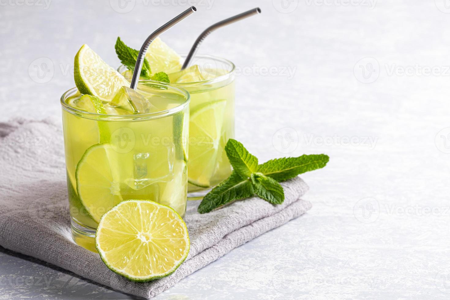 Two glasses with iced green matcha tea with lime, ice, fresh mint and metal drinking straws on light grey backdrop. photo
