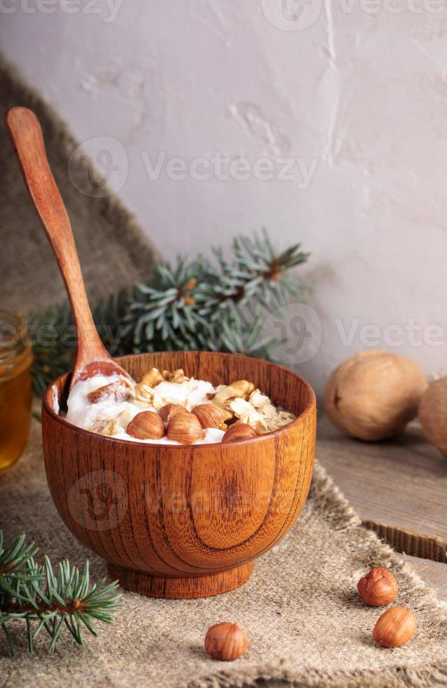 cuenco de madera de yogur con avena arrollada y nueces y cuchara de pie sobre arpillera sobre fondo de pared blanca. foto