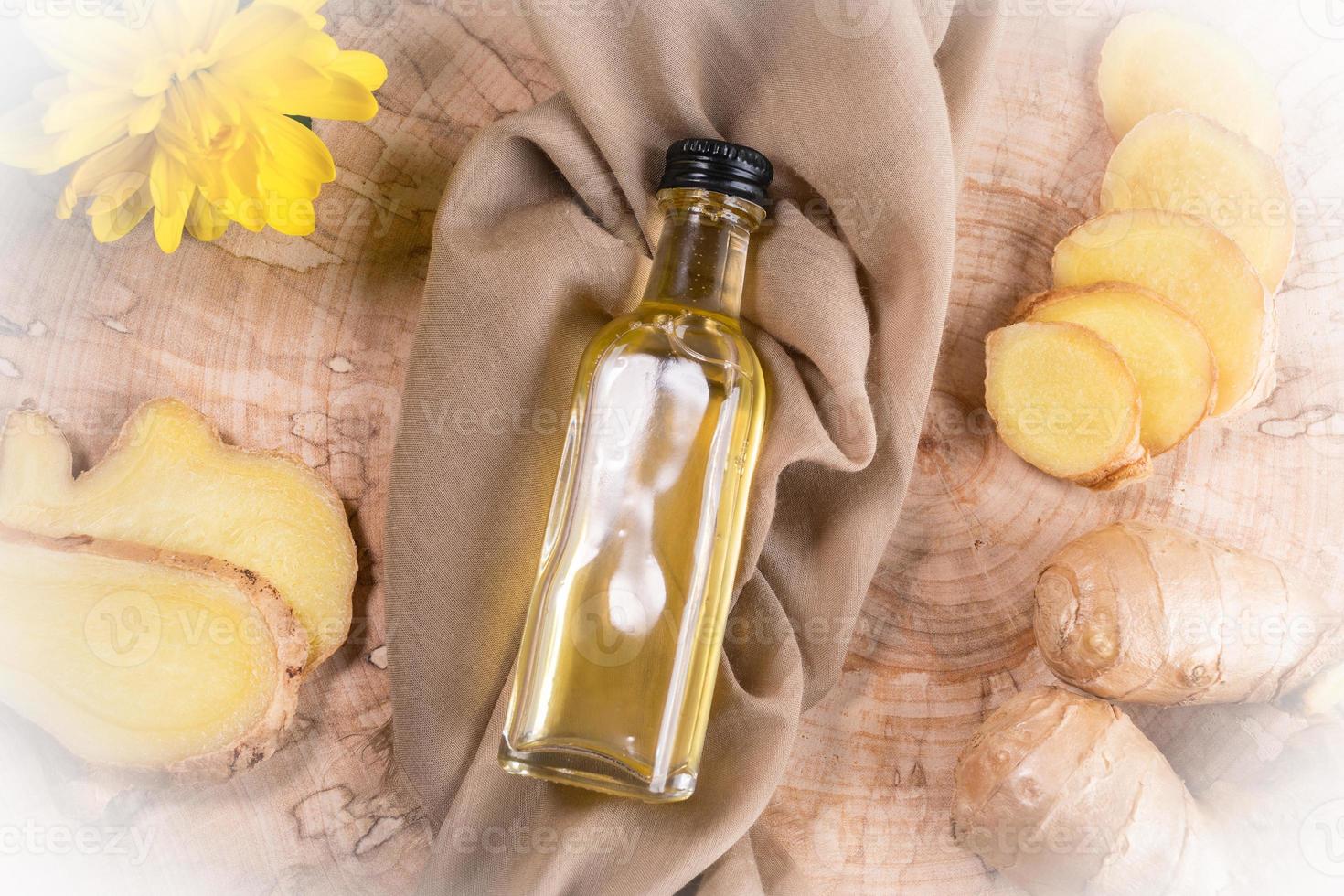 Bottle of ginger oil on cloth In frame of ingredients and flower on wooden saw cut. photo