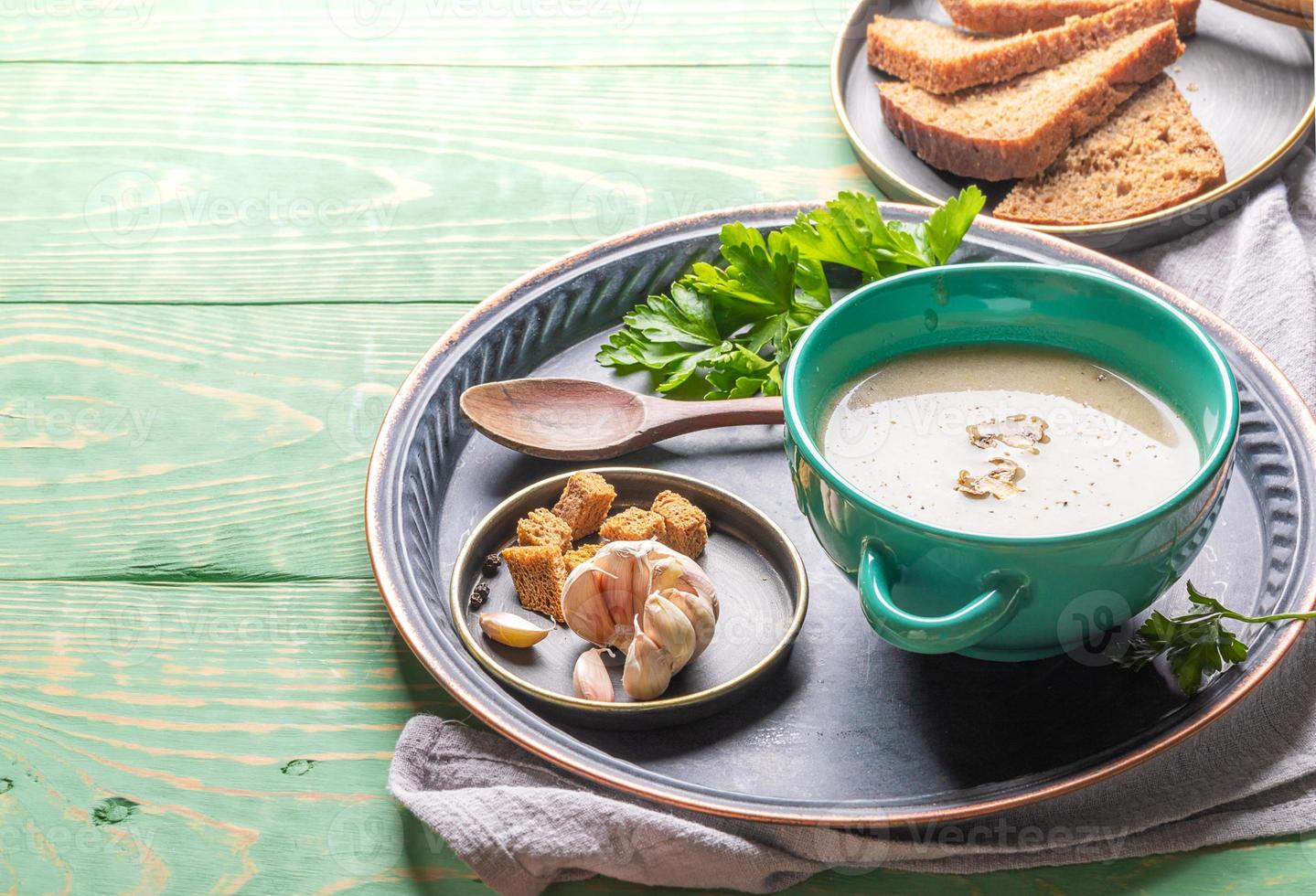 Mushroom cream soup in turquoise ceramic bowl on round metal tray over green wooden background. photo