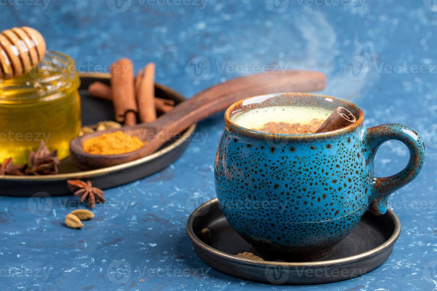 Cup of traditional Indian hot drink golden turmeric milk with cinnamon, turmeric, anise and honey on blue background. photo