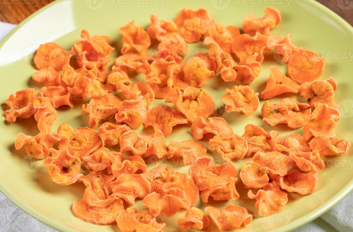 chips de zanahoria caseros naranjas de primer plano en un plato verde redondo. foto
