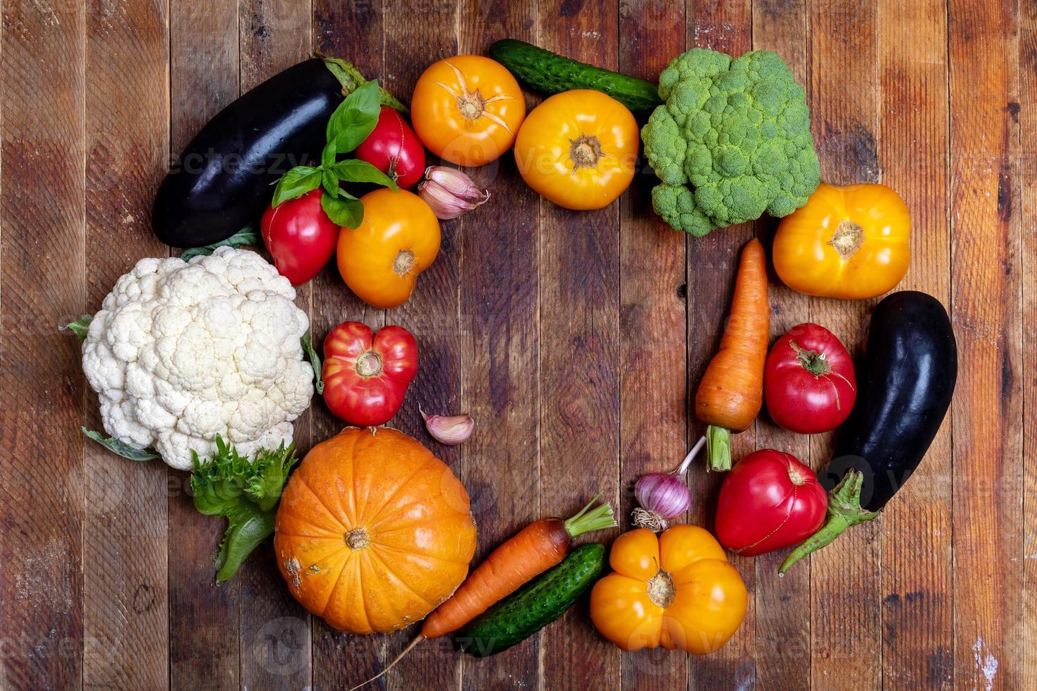 Harvest of fresh farm vegetables is laid out in oval on old rustic wooden table. Top view. Copy space. photo