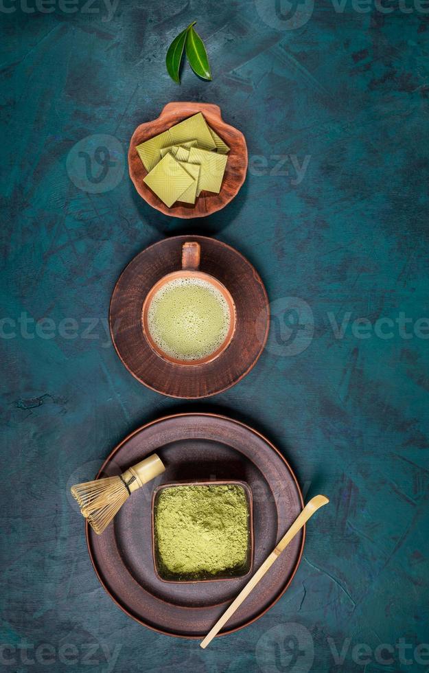 Green matcha tea, powder, chocolate in brown ceramic utensil laid out on emerald backdrop as creative Christmas tree. photo