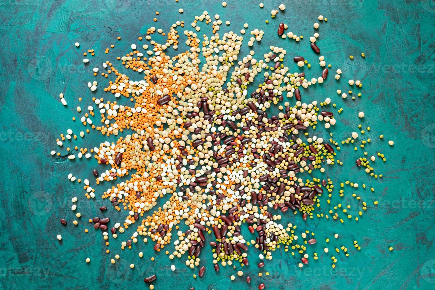 Different beans are scattered from center of emerald green background. Top view. photo