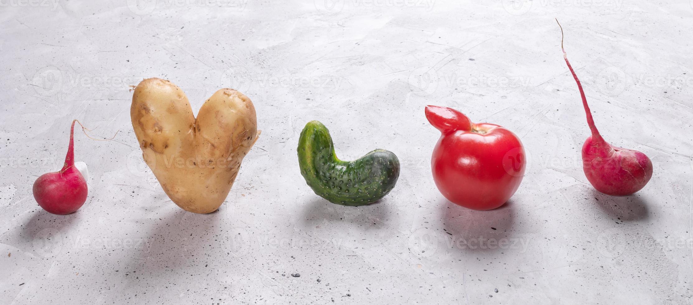 cinco verduras feas están paradas en fila sobre fondo de hormigón gris. foto