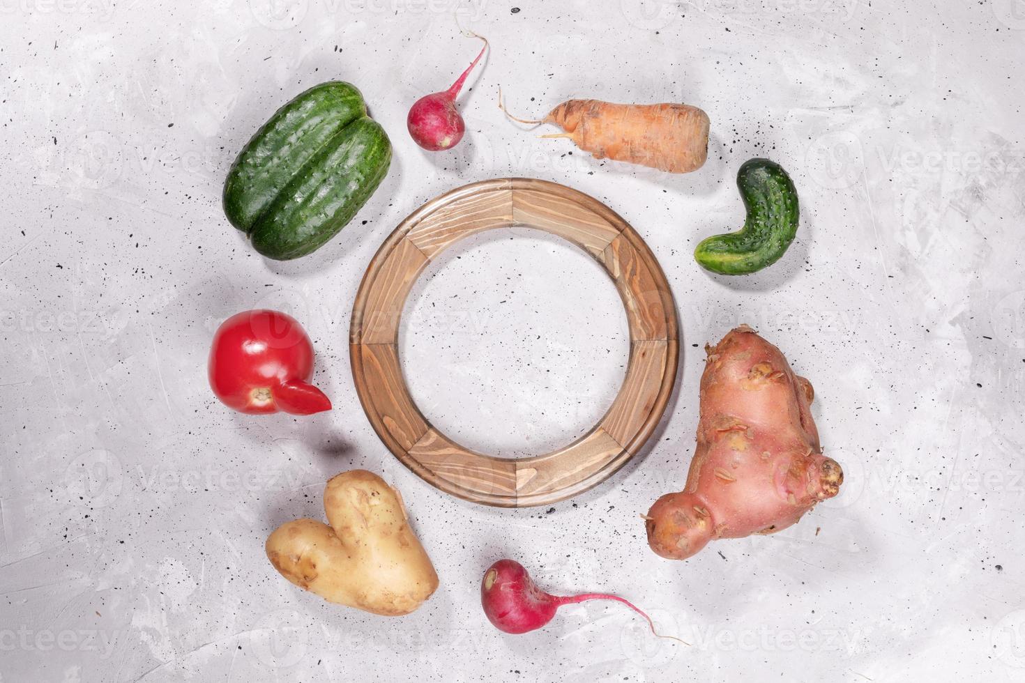 Set of ripe ugly vegetables laid around of rounded wooden frame on grey concrete background. photo