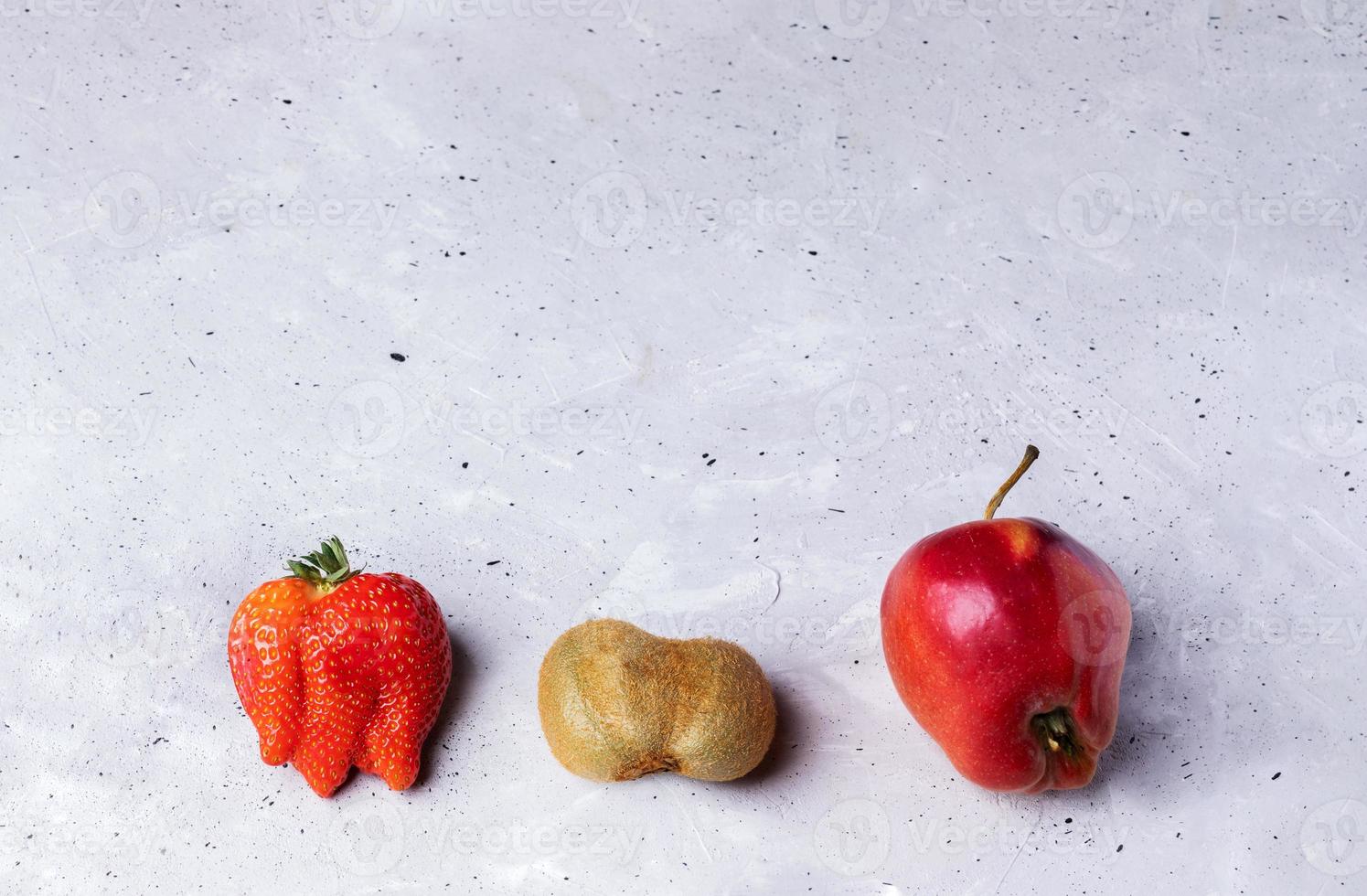 Three ugly fruits strawberry, kiwi and apple on grey concrete background. photo