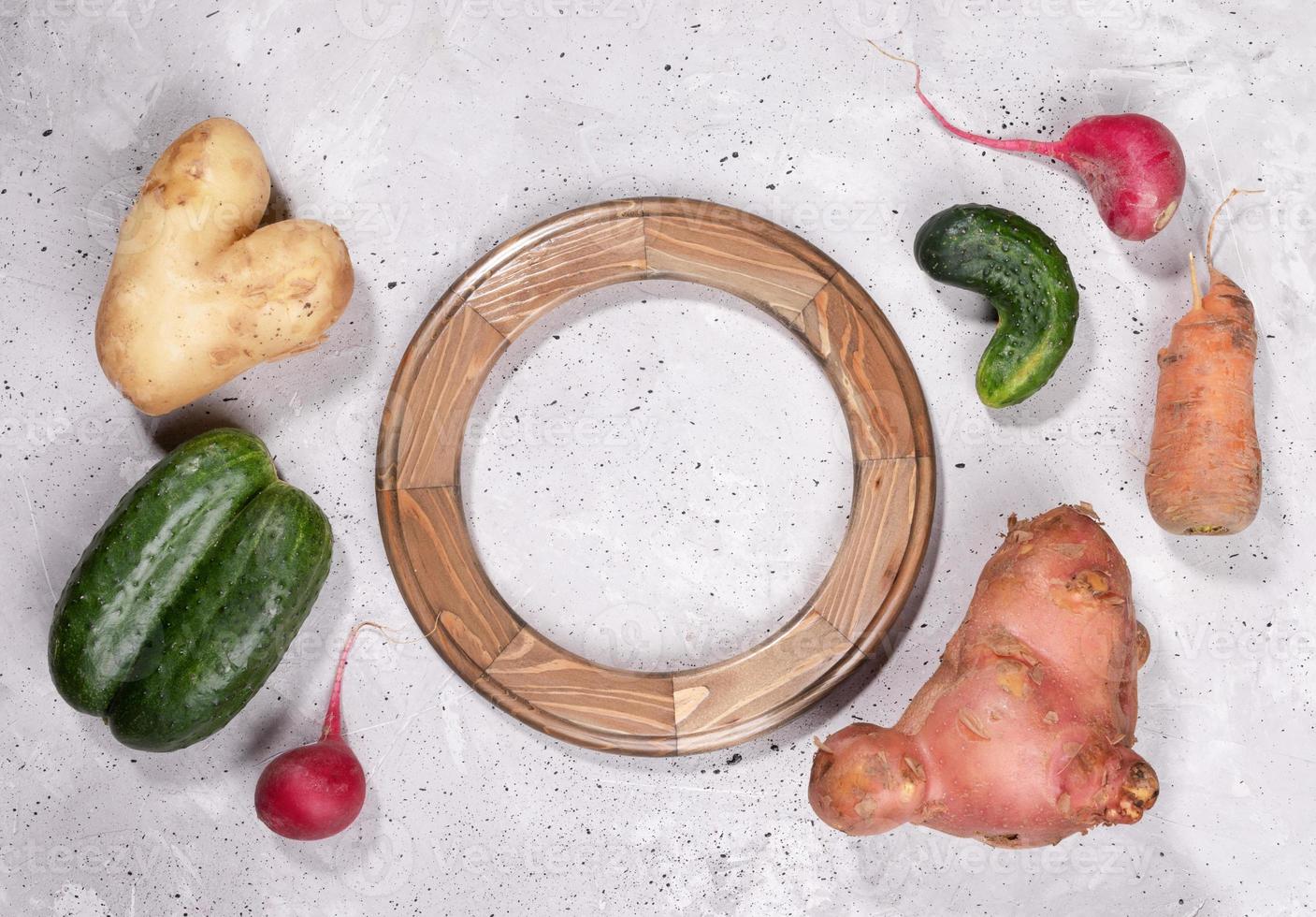Set of ripe ugly vegetables and round wooden frame on grey concrete background. photo