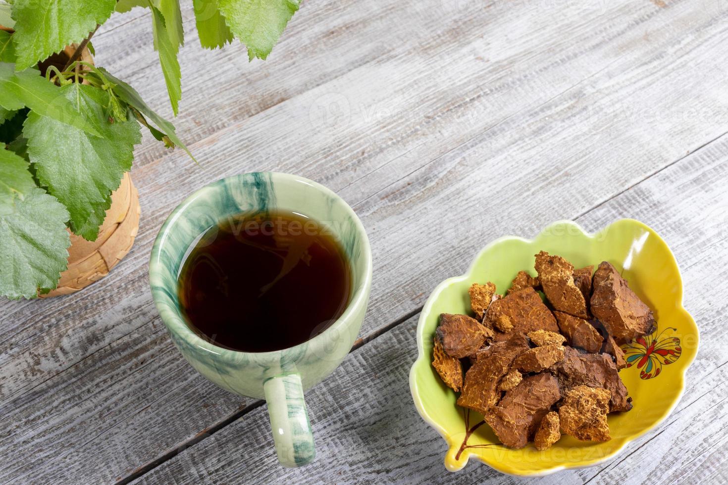 Ceramic cup of healing beverage of birch mushroom chaga and shaped bowl with chaga pieces on light wooden backdrop. photo