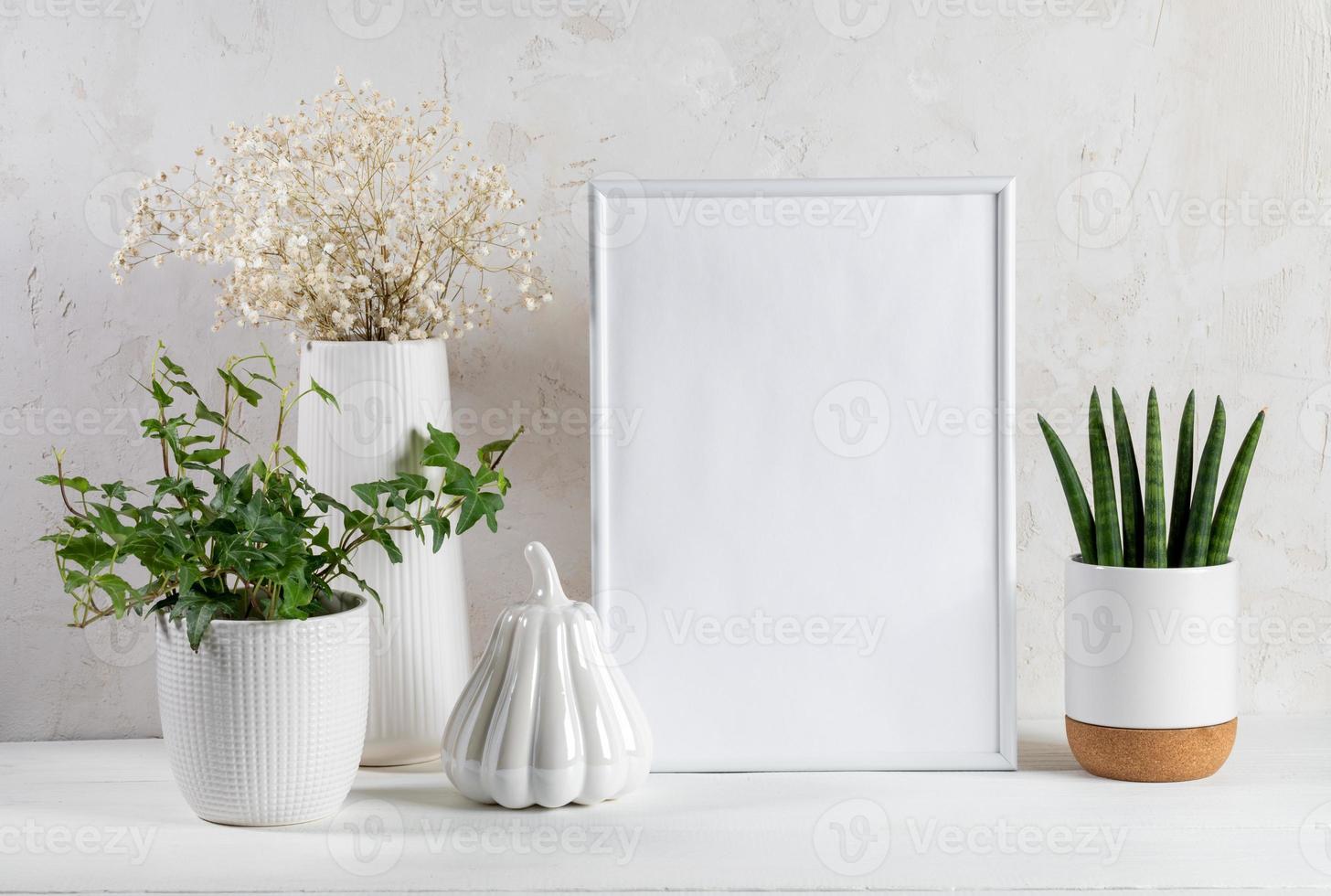 White trendy interior accessories. Frame, artistic pumpkin, houseplants, dry flowers, wooden table. photo