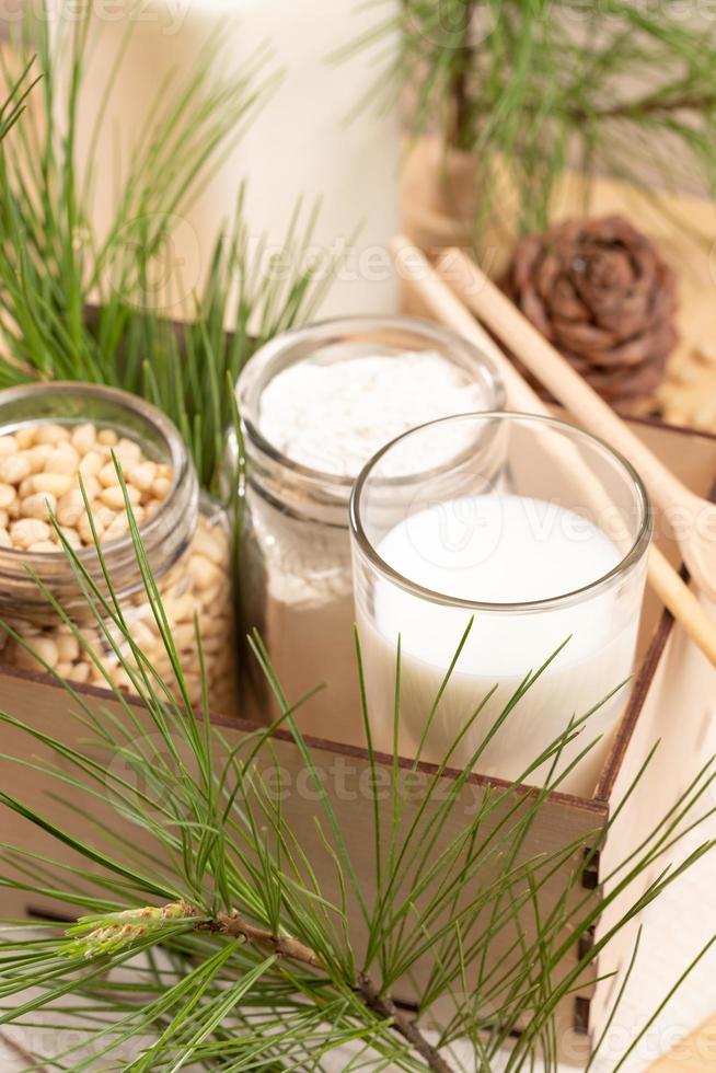 Cedar milk, flour, nuts in glass tableware in wooden box, cone and branches. Selective focus. photo