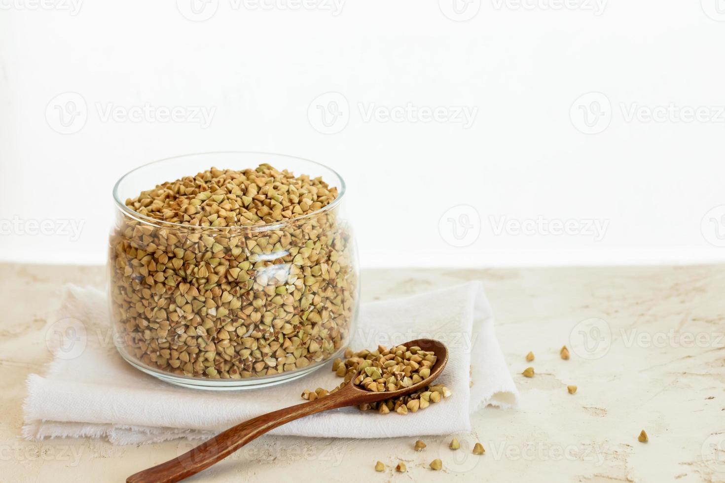 Can of green buckwheat and spoon on table on white background. photo