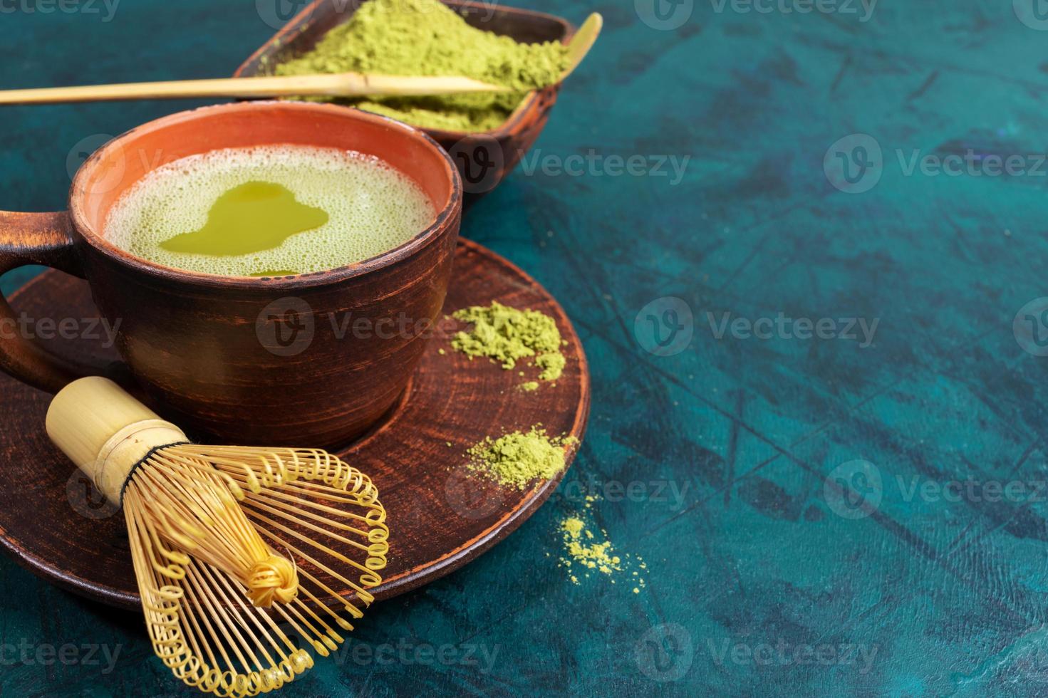 cierre el té matcha verde, el batidor y el polvo en tazas de cerámica marrón sobre fondo esmeralda. copie el espacio para el texto. foto