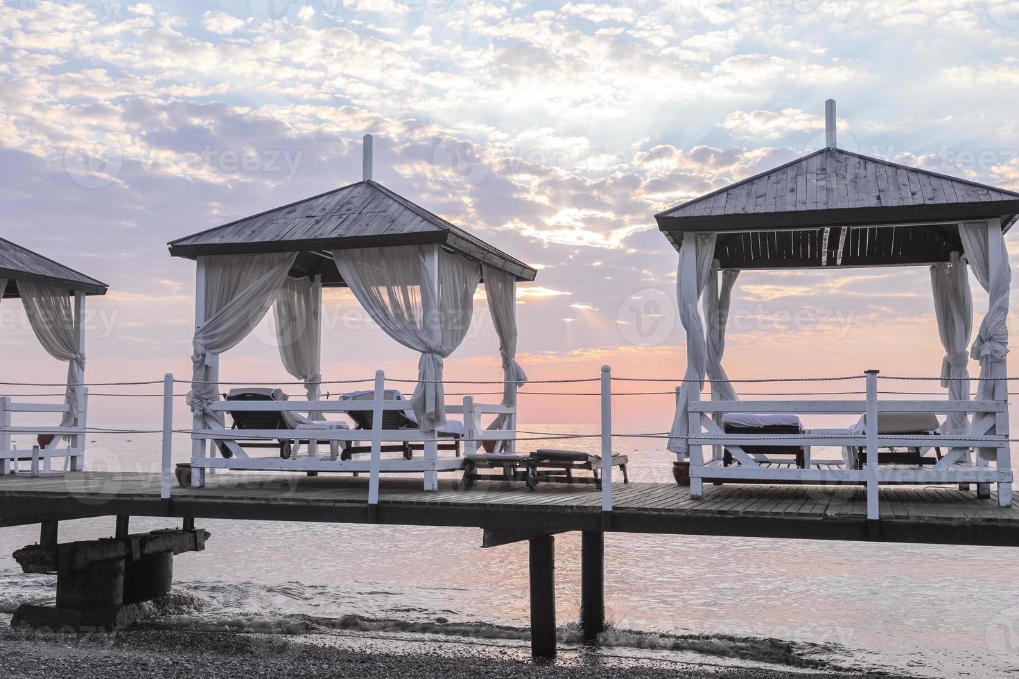 Close-up platform with row of gazebos with sunbeds at dawn. photo