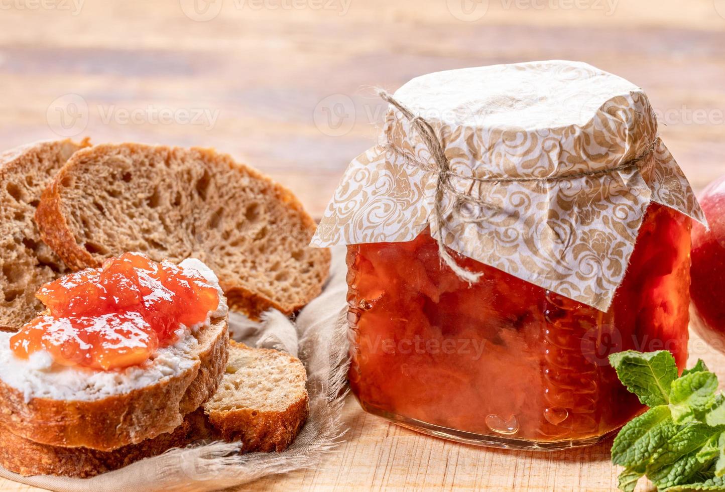 Close-up glass jar full of apple jam, sliced  bread, smeared with curd and apple jam on wooden background. photo