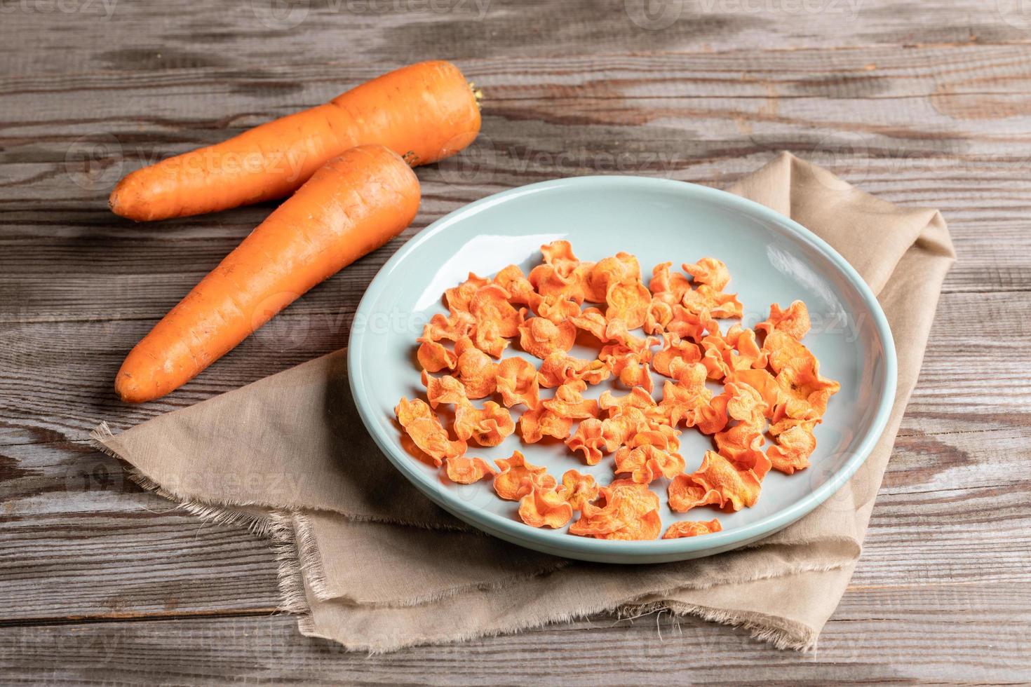 Round turquoise plate with carrot chips on beige fabric and two whole carrots on wooden table. photo