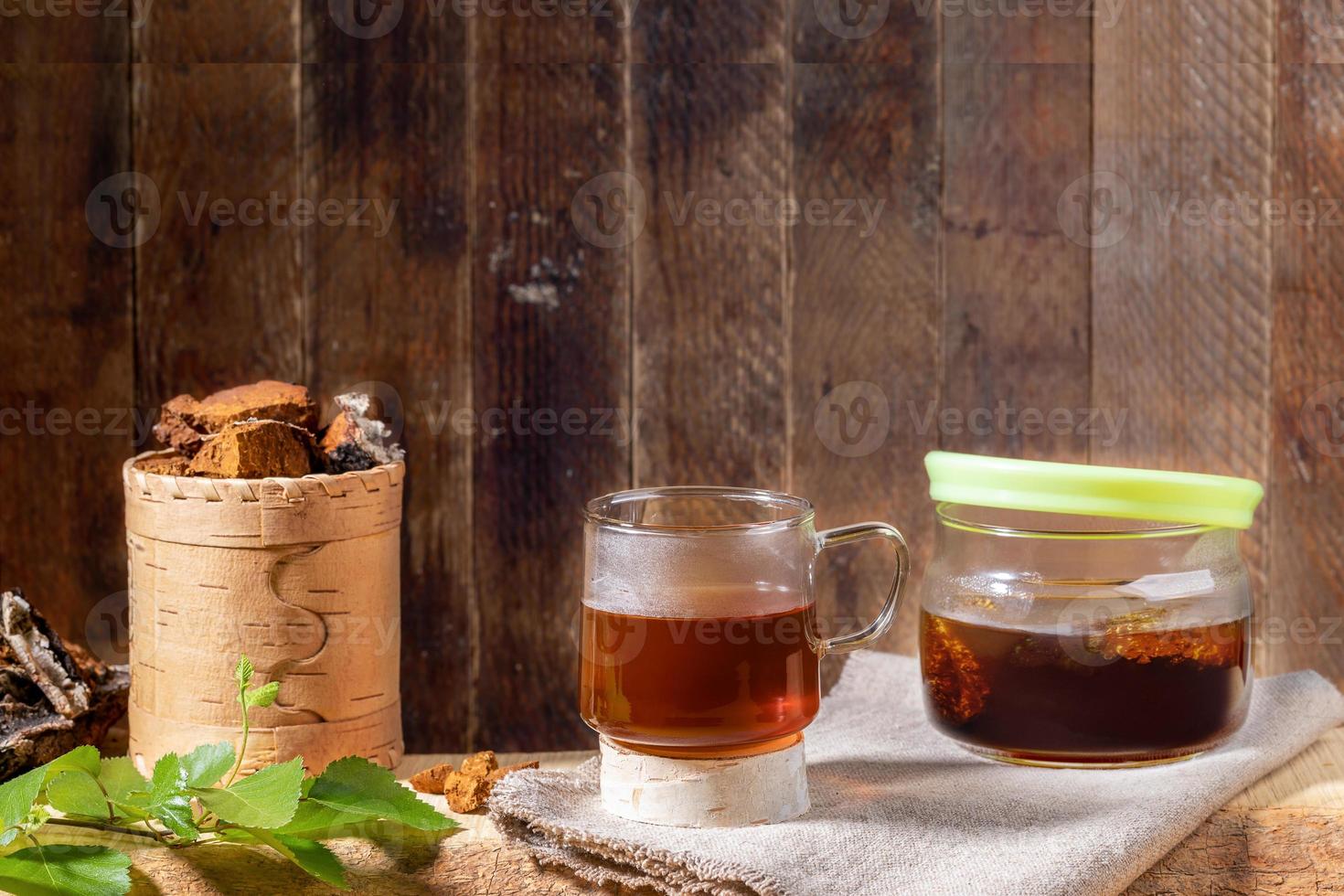 Healing beverage from birch mushroom chaga, mushroom pieces, twig on wooden plank on old wooden backdrop. Copy space. photo