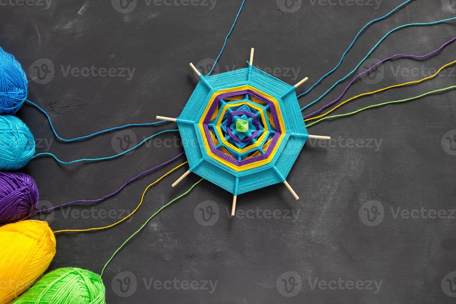 Handmade mandala and multicolored threads on dark grey background. photo