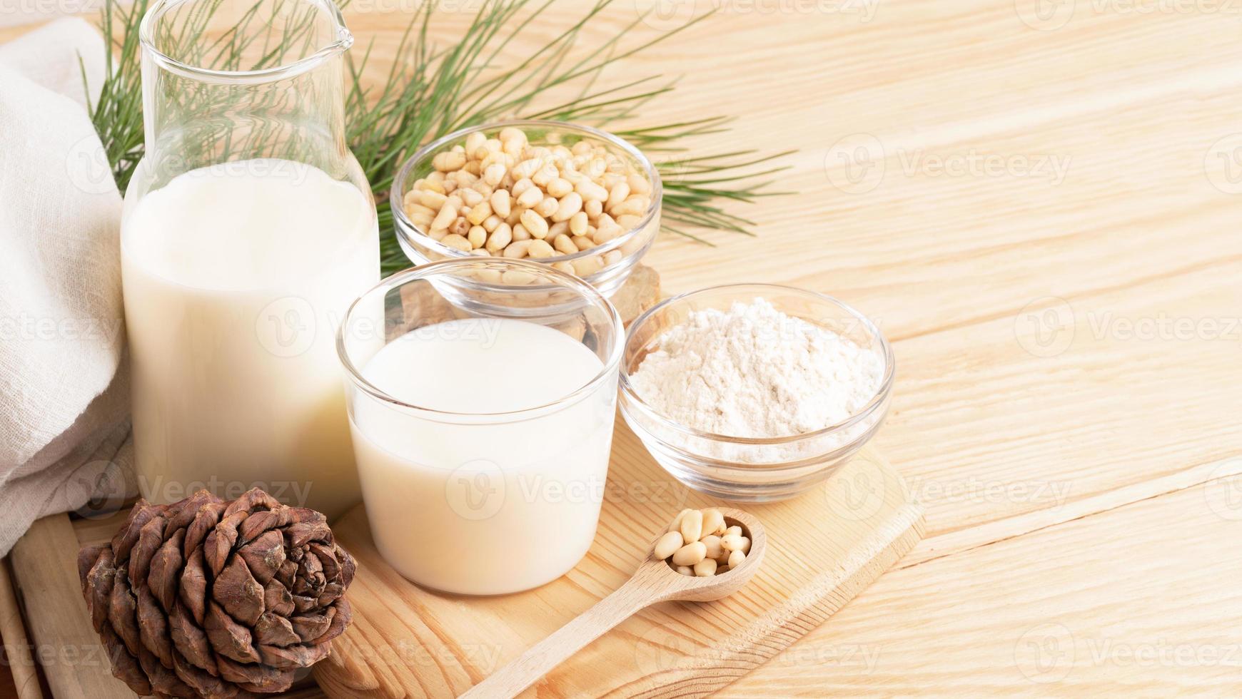 Cedar milk, flour, nuts in glass tableware, cone, branch on wooden table. Banner. Copy space. photo