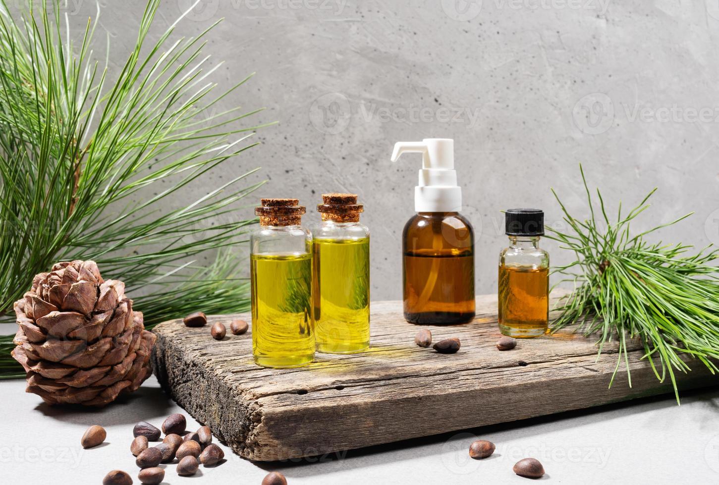 Composition of small glass bottles of essential cedar oil on old wooden board, cedar branches, cone and nuts on grey. photo