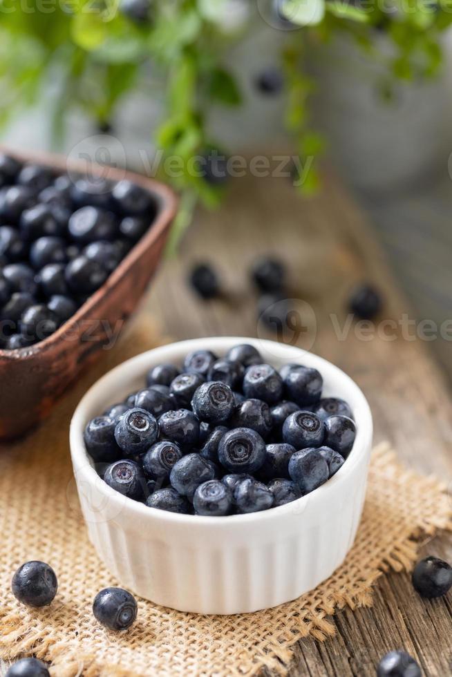 Wild blueberries in white bowl on burlap on wooden table. Natural superfood with vitamins. photo