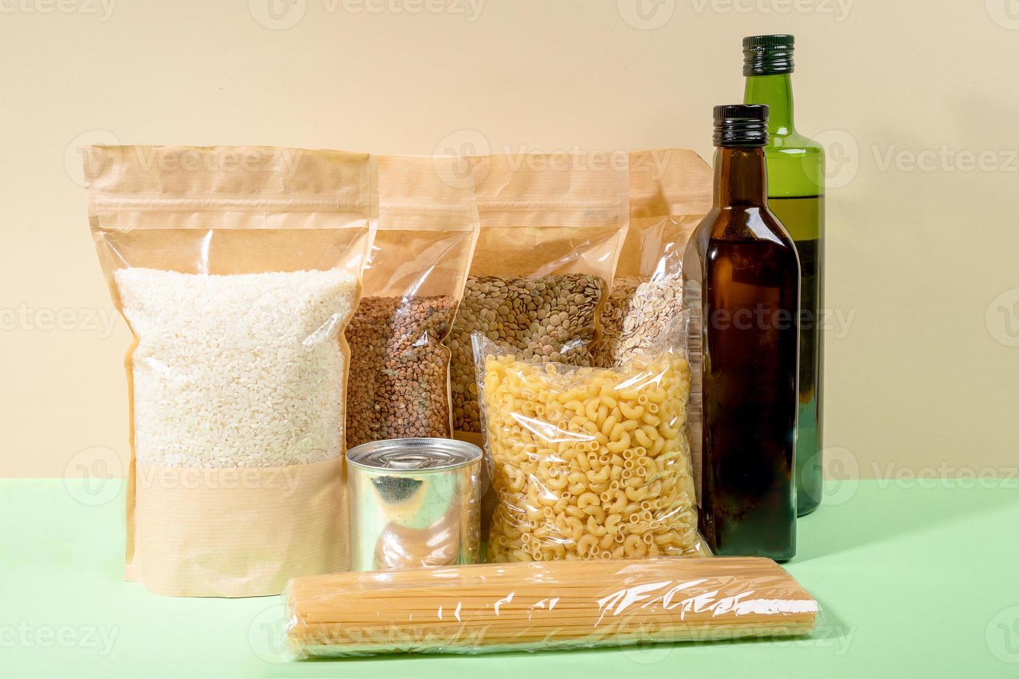 Stock of food products in paper and cellophane packagings on beige-green backdrop. Cereals, pasta, oil bottles. Closeup. photo