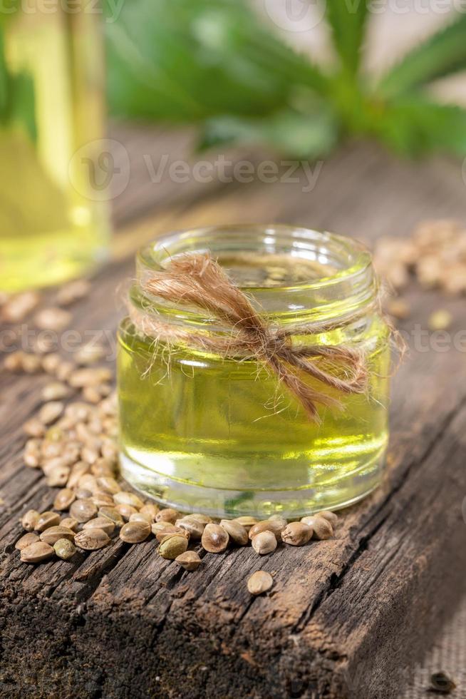 Hemp oil in glass jar and grains of cannabis on old wooden board, bottle with oil and leaves are blurred. photo