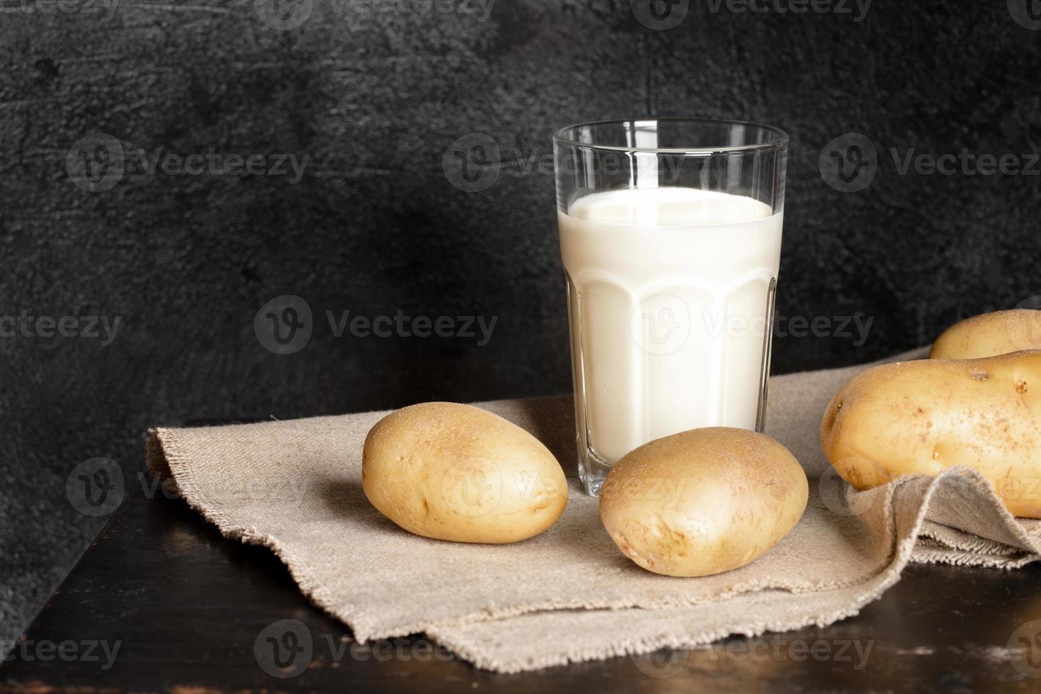 Glass with organic drink from potato and potato tubers on black background. Selective focus. photo