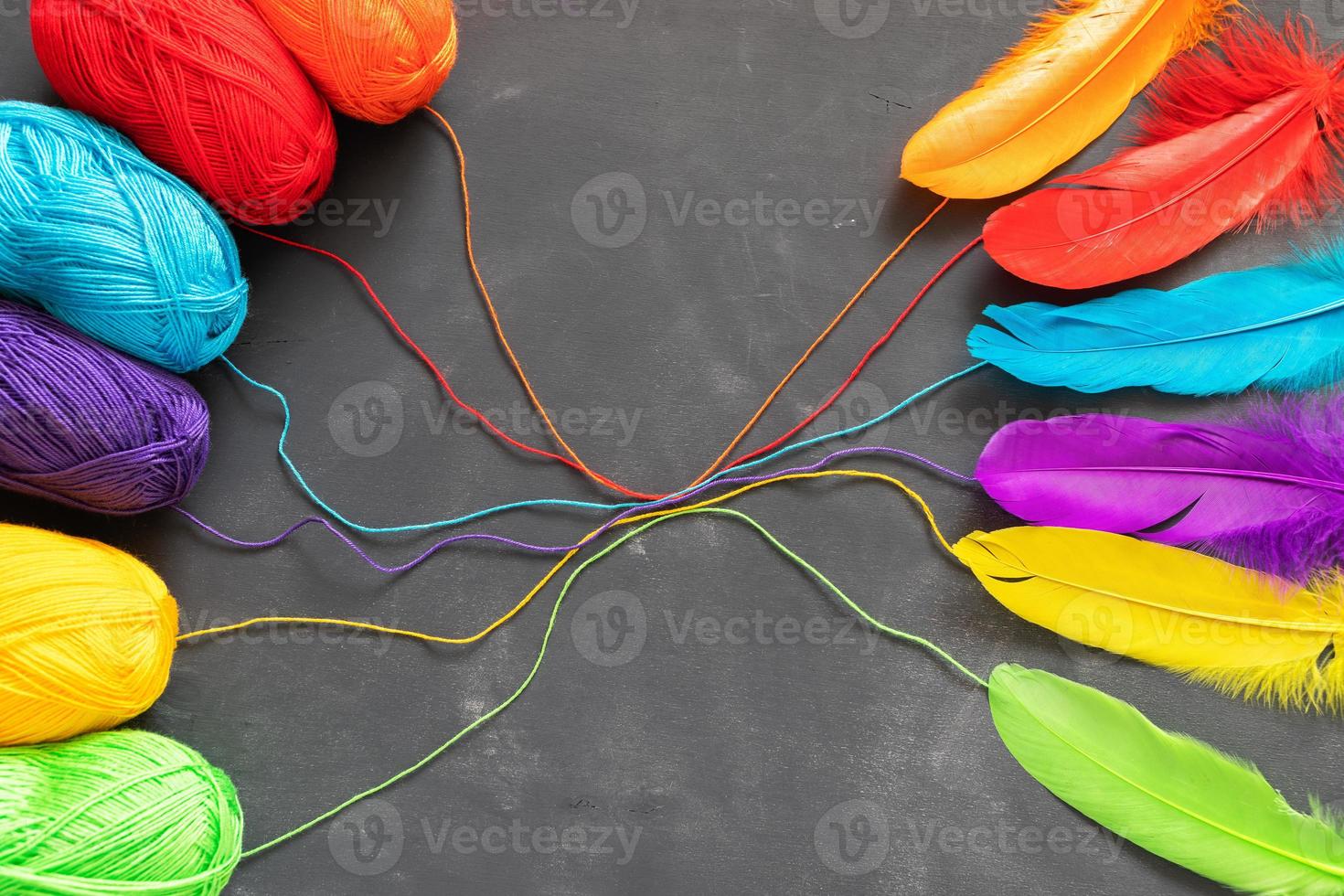 Colored yarn thread skeins and multicolored feathers on dark grey background. photo