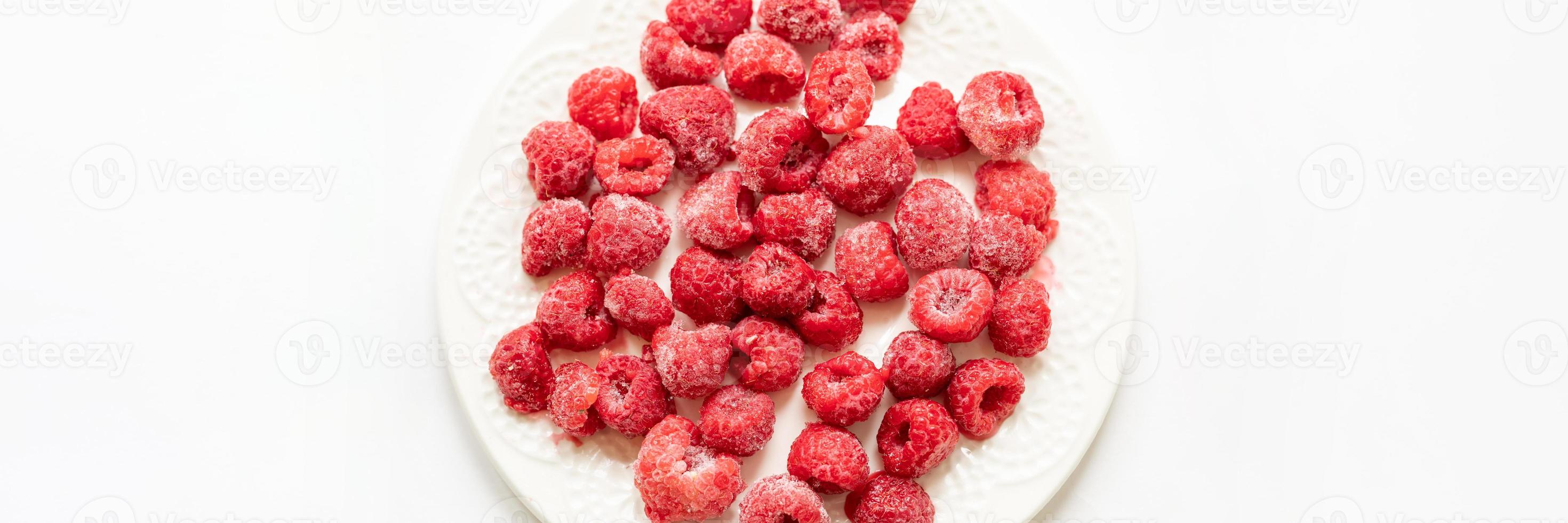 Frozen raspberry on white plate in white background. Banner. View from above. Copy space. photo