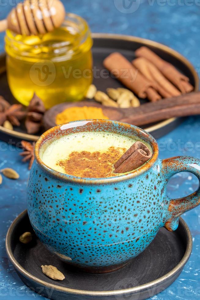 Blue cup of traditional indian ayurvedic golden turmeric latte milk with ingredients on blue background. Selective focus. photo