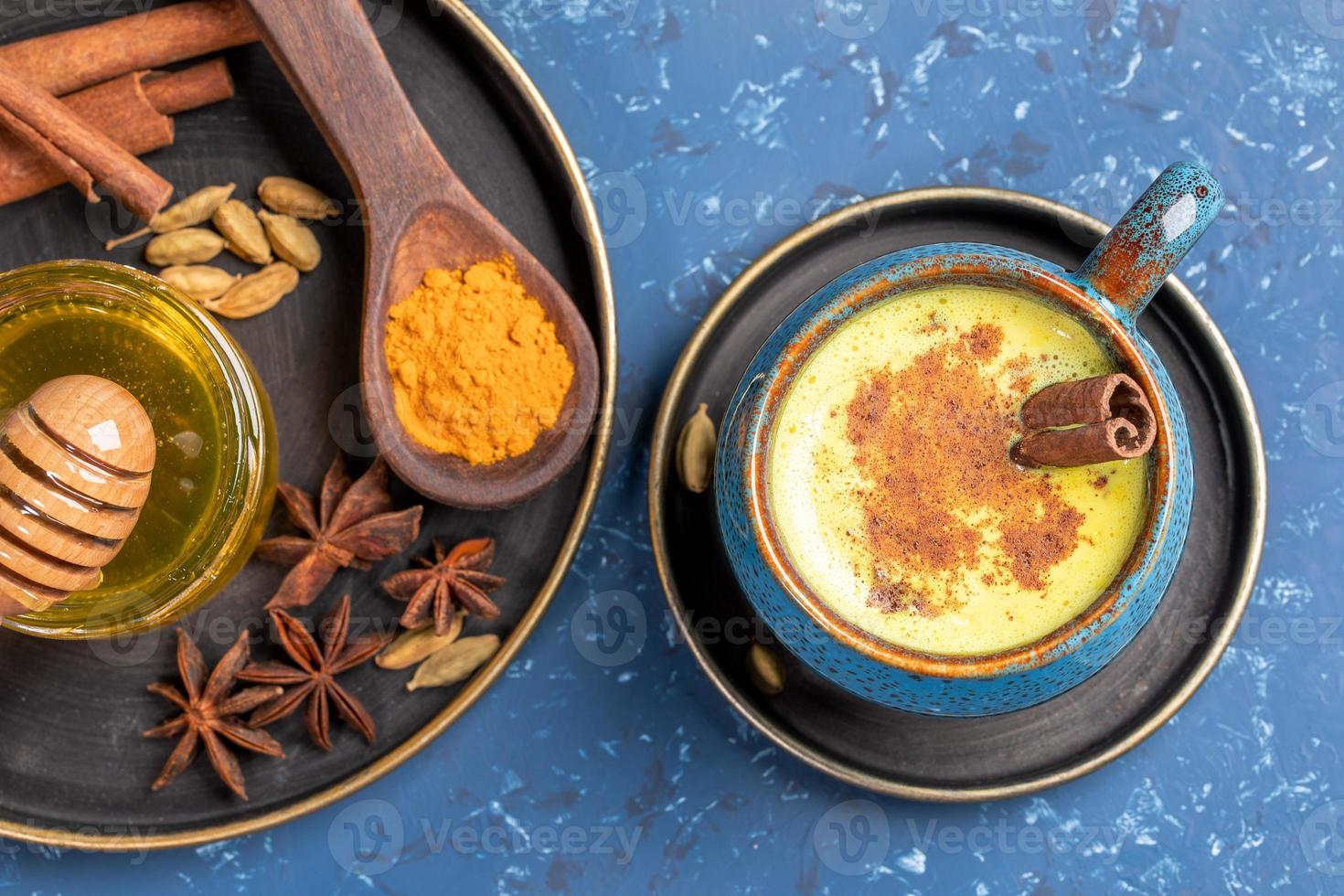 Top view of cup of traditional Indian ayurvedic golden turmeric milk and plate with ingredients on blue background. photo