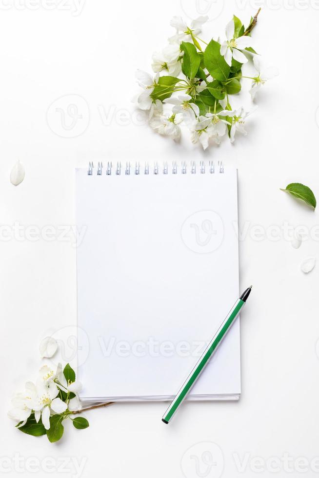 White empty notebook with pen, white apple tree flowers white background. Top view. photo