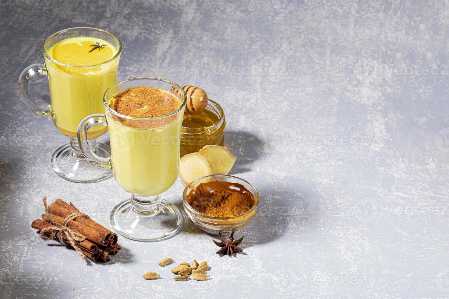 Turmeric milk for immunity. Two glasses for mulled wine with golden milk with ingredients on light grey background. photo