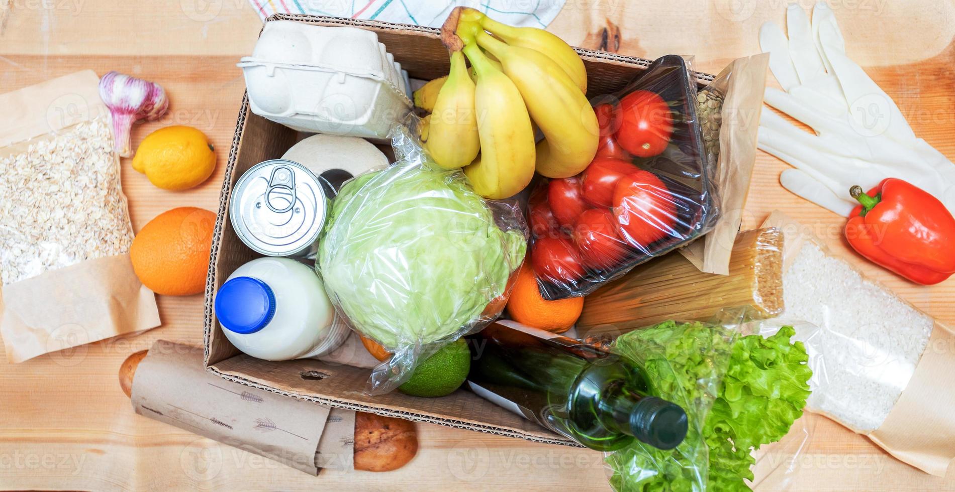 productos alimenticios recién entregados en caja de cartón y sobre mesa de madera. entrega segura. donación de alimentos. vista superior. foto