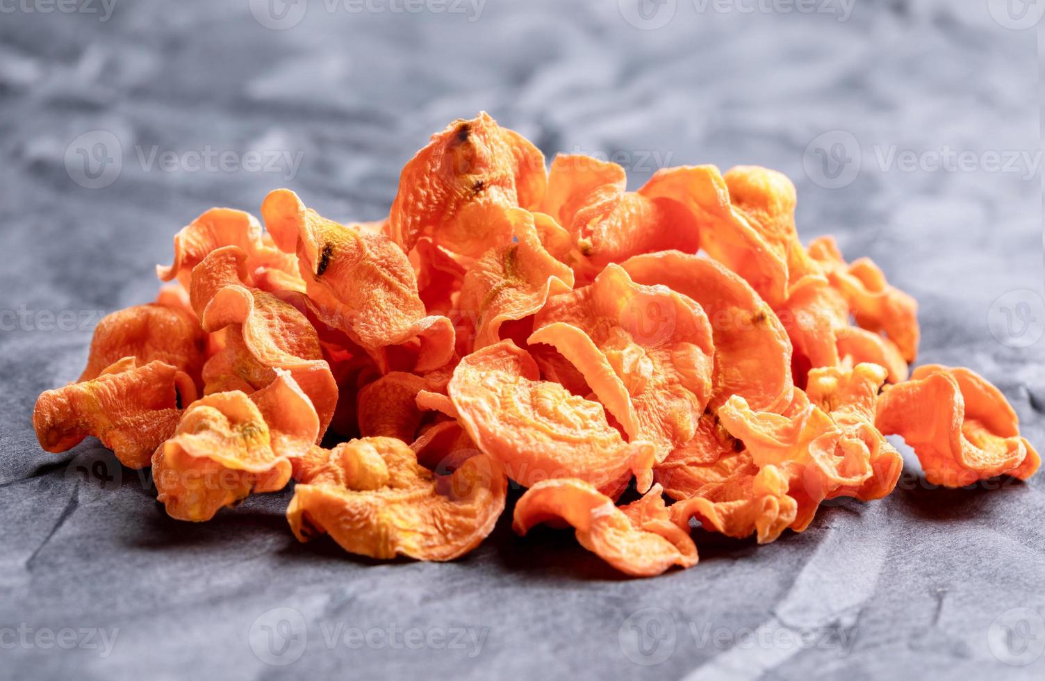 Front view to small bunch of orange carrot chips on rumpled black paper. photo