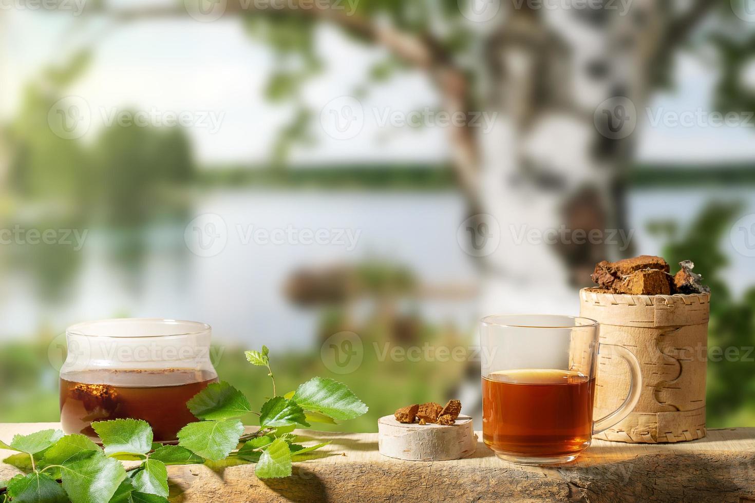 Healing beverage from birch mushroom chaga and chaga mushroom pieces on blur backdrop of birch tree near lake. photo