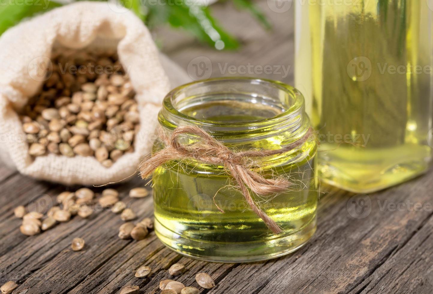 aceite de cáñamo de primer plano en frasco de vidrio y botella con granos de cannabis en saco sobre tabla de madera. foto