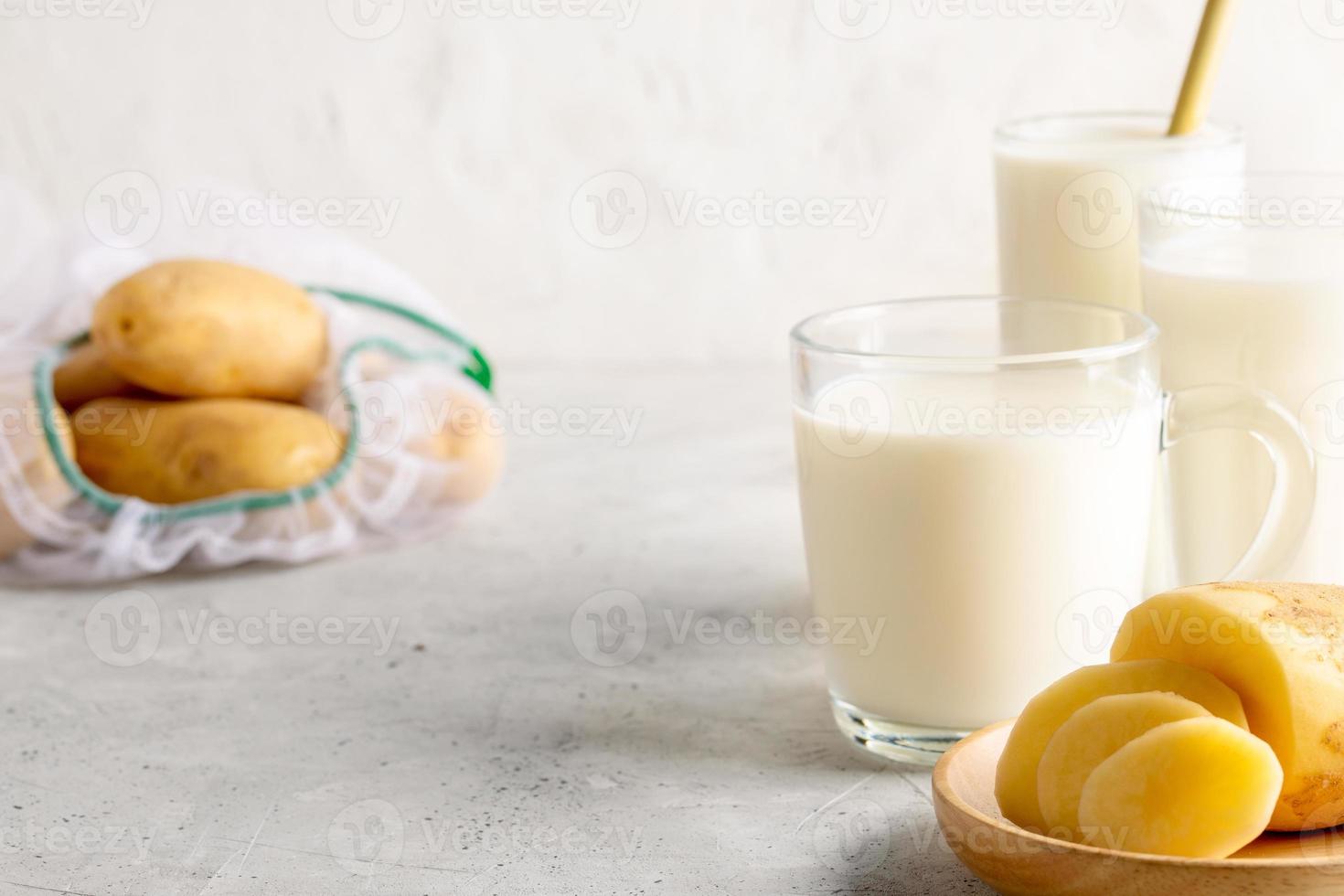 leche vegetal de patata vegana en vasos y tubérculos de patata sobre fondo de hormigón con espacio para copiar. foto