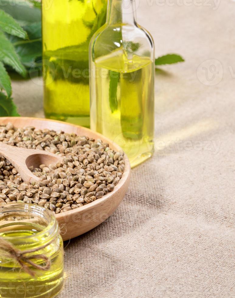 Hemp products oil in glass jar and bottle, cannabis graines in round wooden plate on burlap napkin. photo