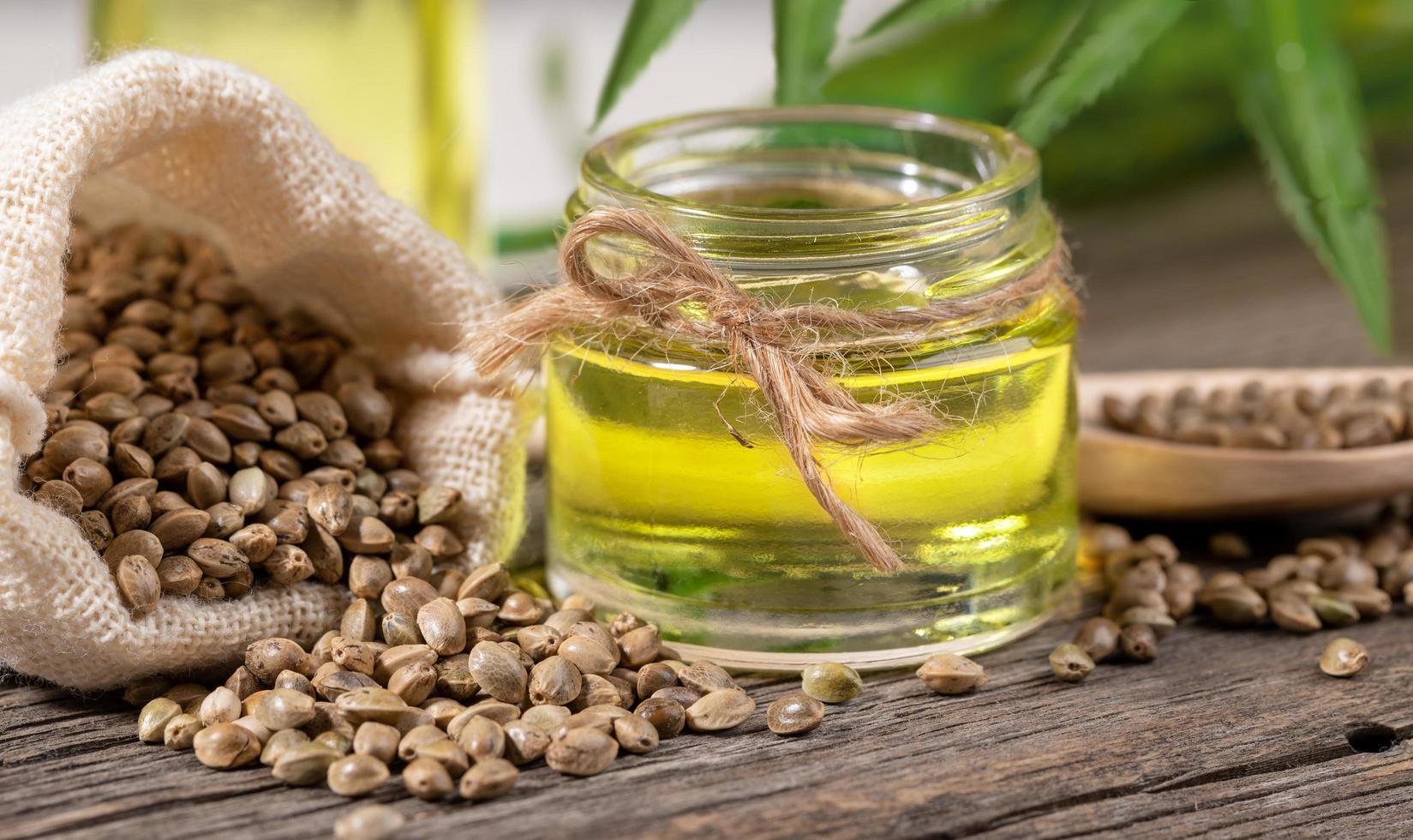 Close-up glass jar with hemp oil and cannabis seeds in sack and in wooden spoon on old wooden board. photo