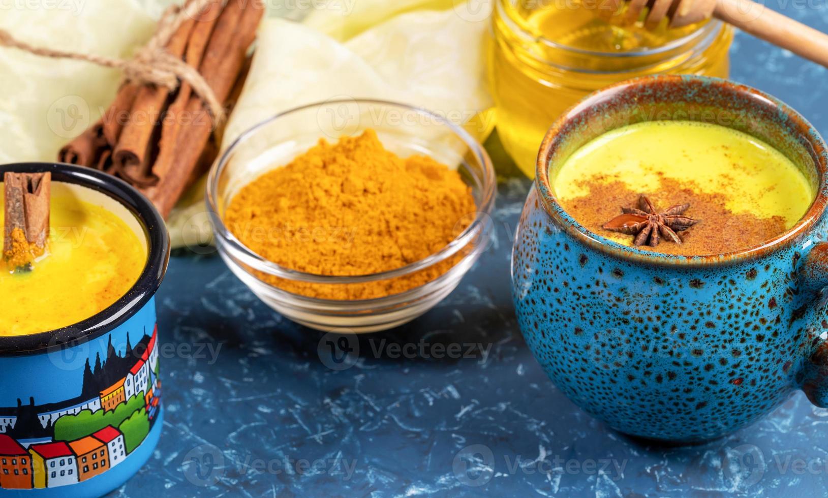 Cups of golden turmeric milk with cinnamon. Ingredients. Yellow napkin and blue backdrop. Close-up, selective focus. photo