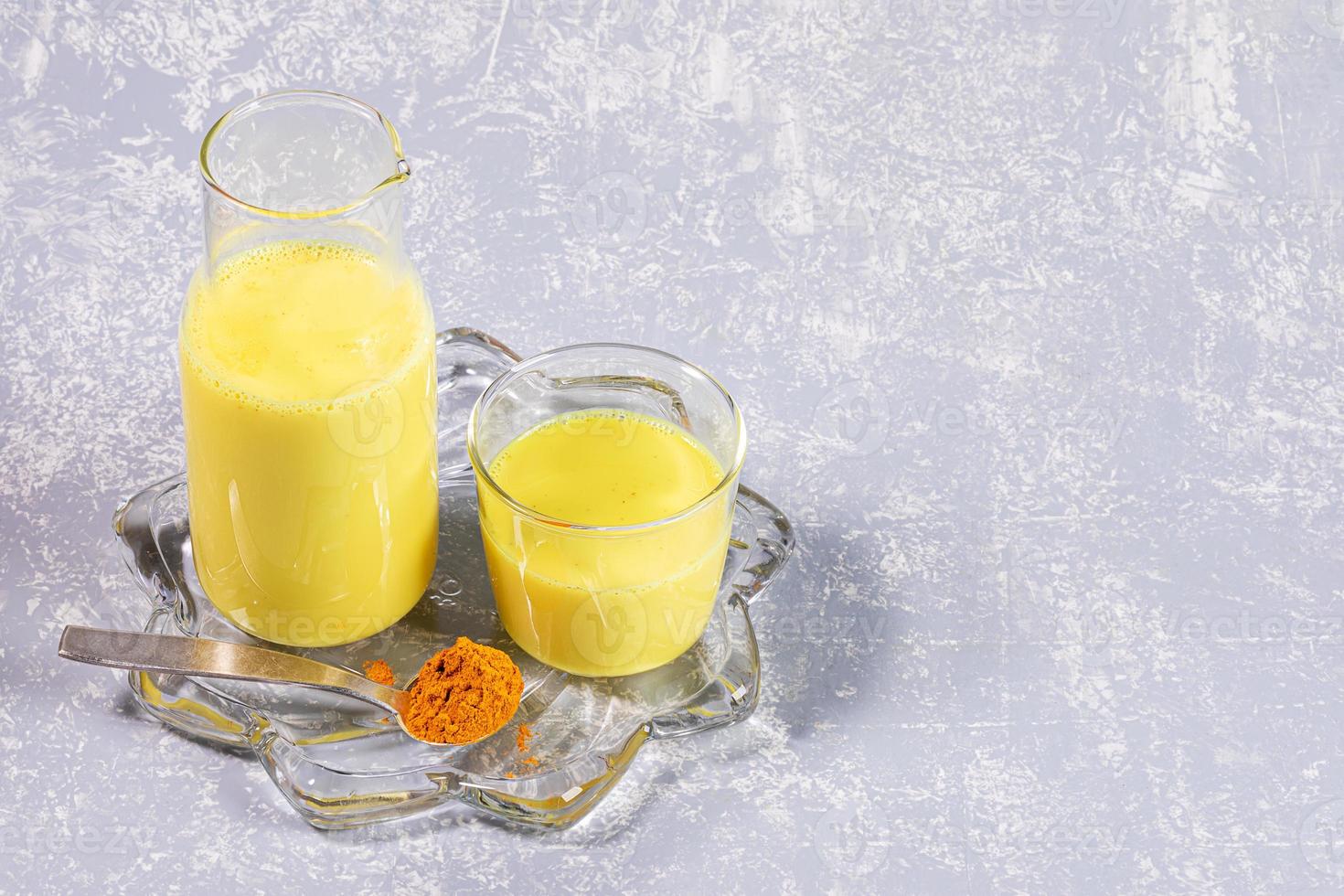 Organic turmeric milk. Bottle and glass with golden milk on figured transparent plate on light grey background. photo