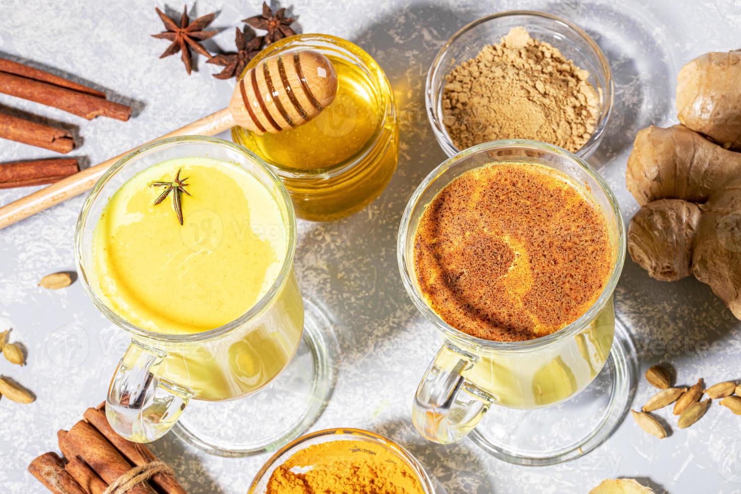 Organic turmeric milk. Two glasses for mulled wine with golden milk with ingredients on light grey backdrop with shadows. photo