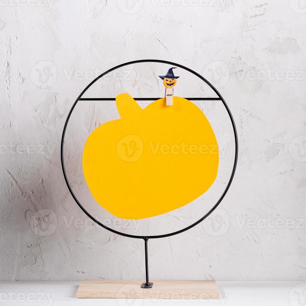 Minimal Halloween image with empty yellow sheet in form of pumpkin on metal stand. Copy space. photo