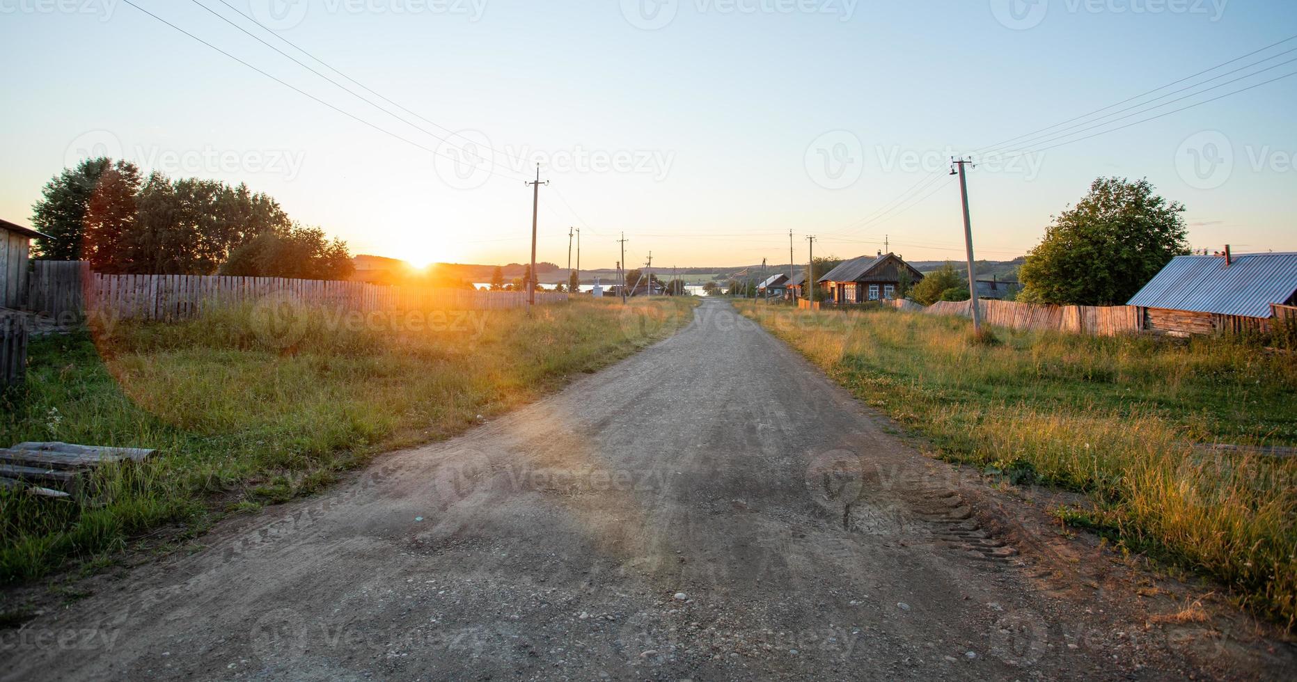 Sun-drenched ground road leading to river in village at sundown in Russia. photo