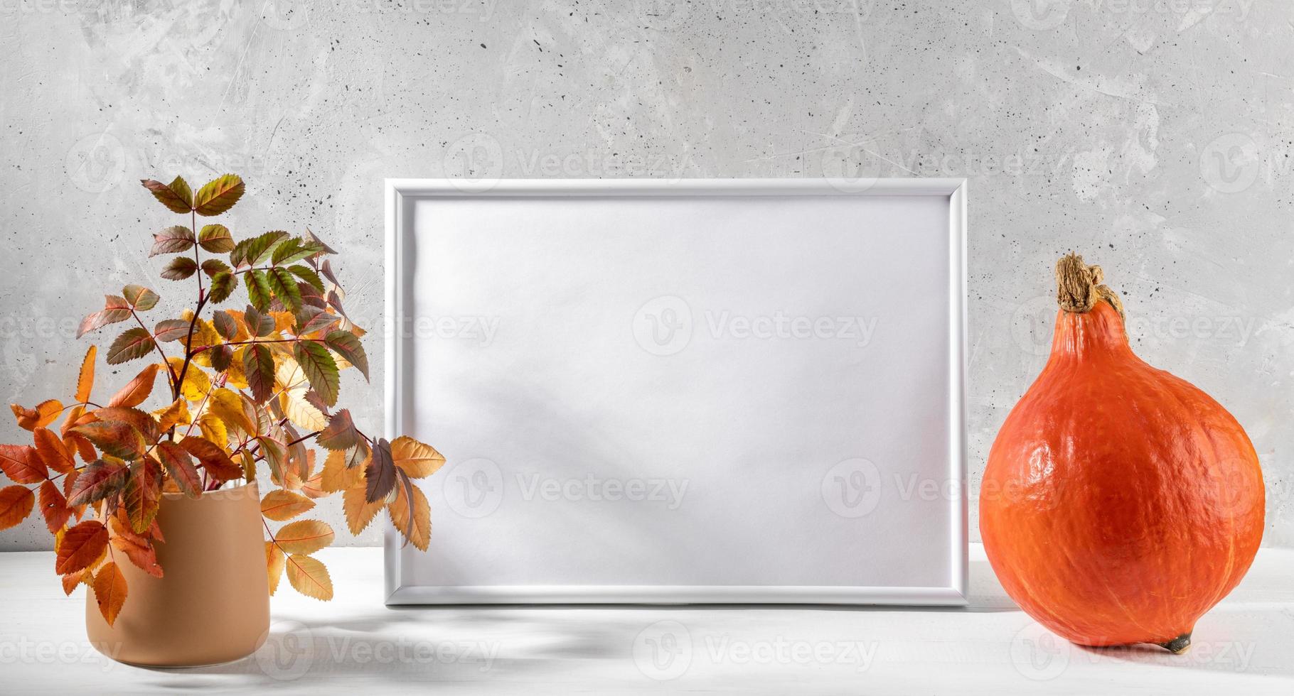 Fall composition with orange pumpkin, empty white frame and color leaves on light background. photo